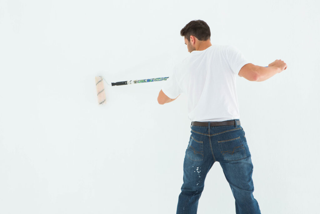 Rear view of man using paint roller on white background